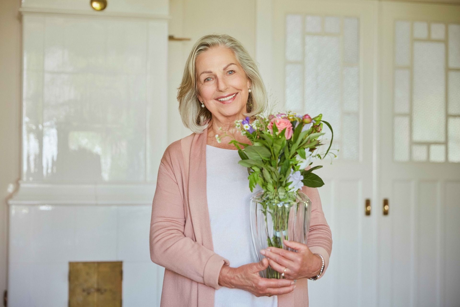Frau im Rentenalter steht mit Blumen in der Küche und lächelt