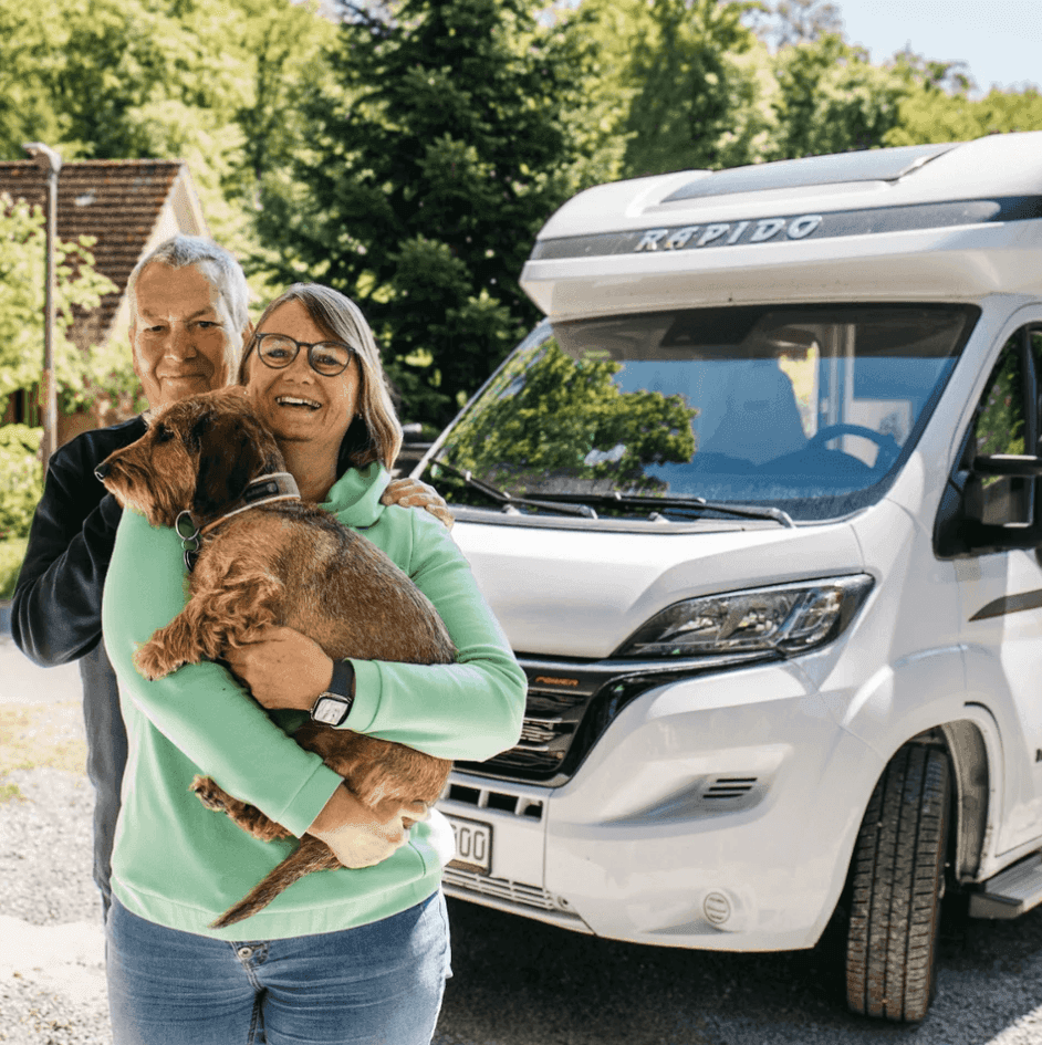 Ehepaar mit Hund steht vor ihrem Wohnmobil